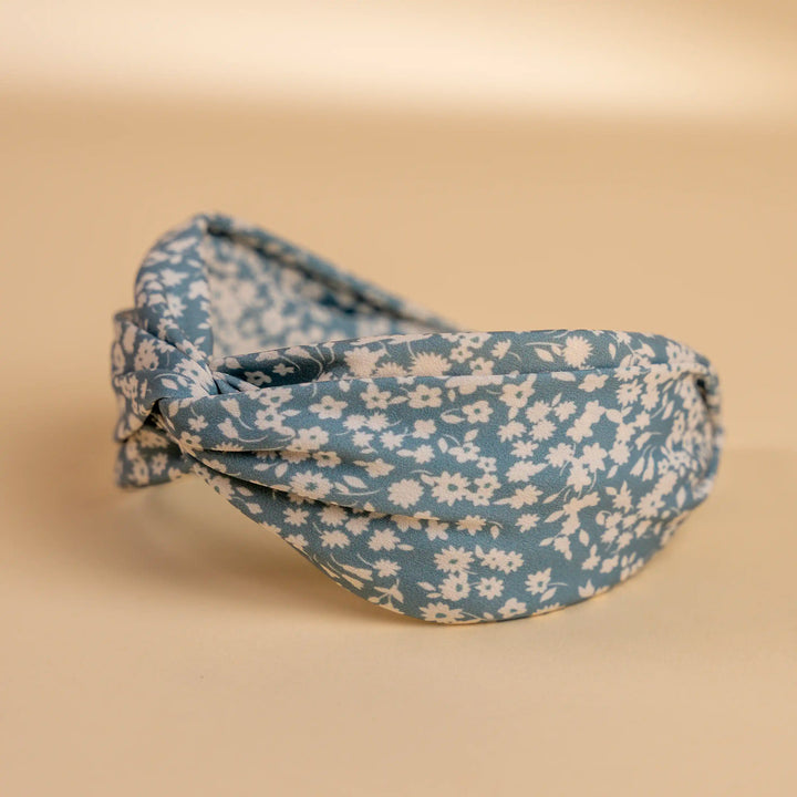 Lucys blue and white simple floral headband. Light blue background with simple white floral pattern. Side view.