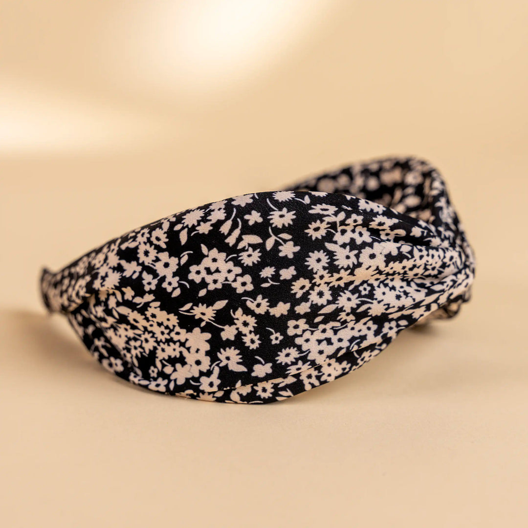 Lucys black and white simple floral headband. Black background with simple white floral pattern. Side view.